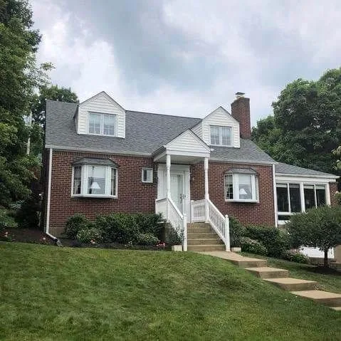Brick home on a hillside lot with completed roofing and gutters