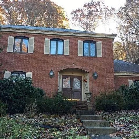 Brick two-story home with new windows and roofing surrounded by trees